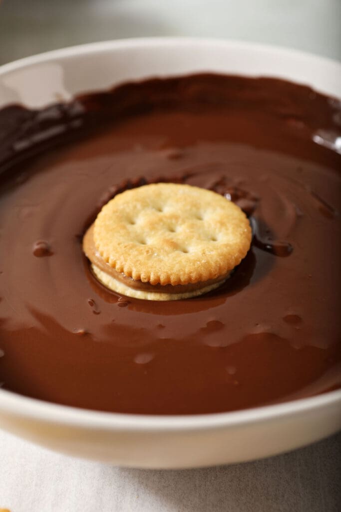 A ritz cracker sandwich with peanut butter in a bowl of melted chocolate, before coating