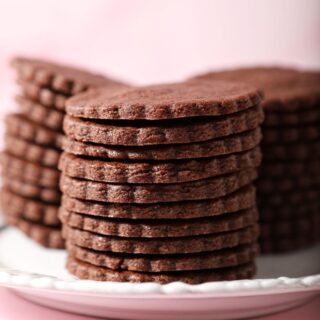 Three tall stacks of round Chocolate Sugar Cookies on a white plate on a pink surface