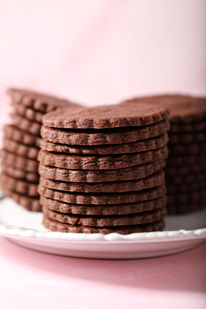 Three tall stacks of round Chocolate Sugar Cookies on a white plate on a pink surface