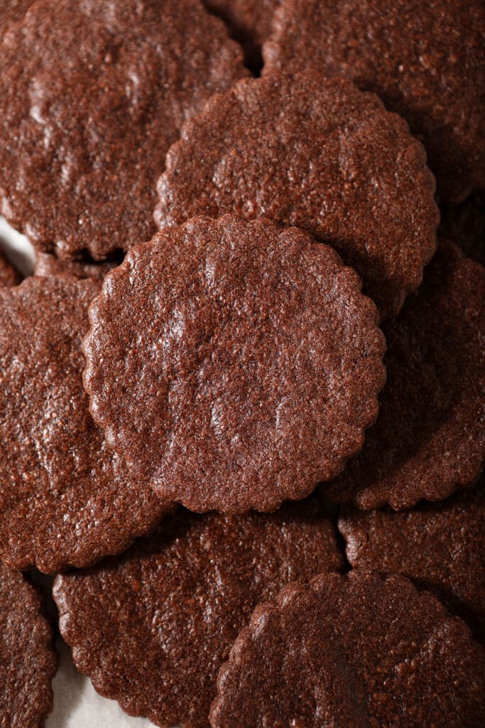 Several scalloped chocolate sugar cookies on a sheet pan stacked on top of each other