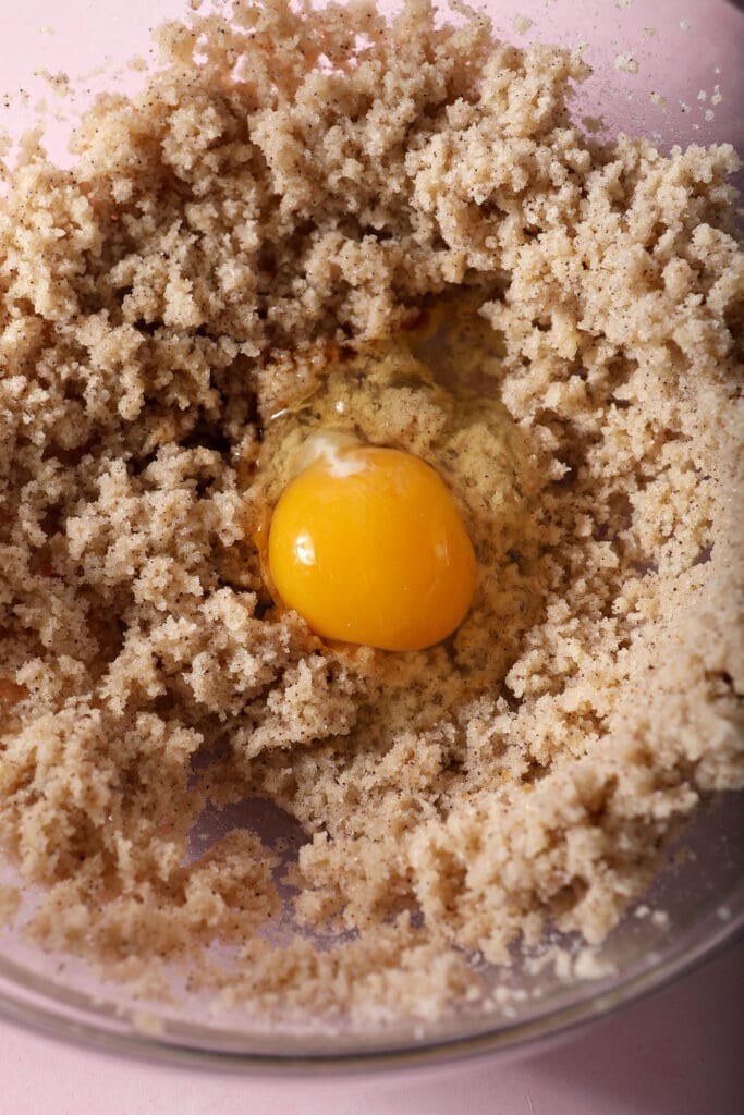 An egg and vanilla extract on top of a butter-sugar mixture in a bowl