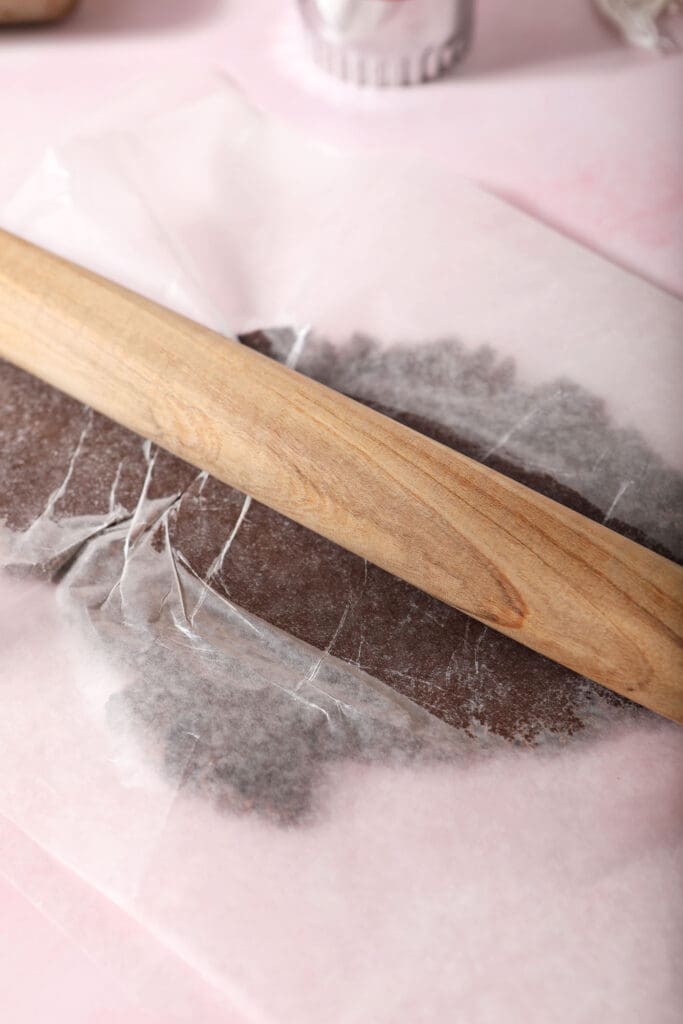 A rolling pin rolls out chocolate sugar cookies between wax paper