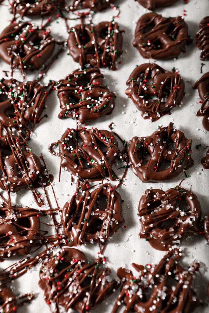 Chocolate Covered Pretzels covered in Christmas sprinkles on a parchment-lined sheet pan while cooling