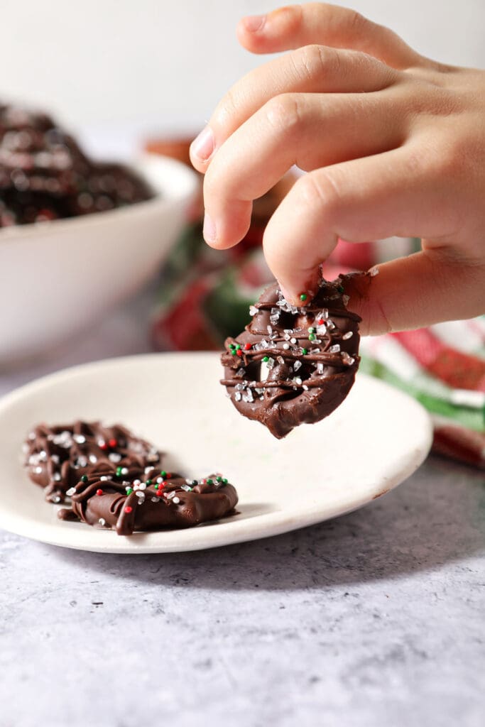 A child picks up a chocolate covered pretzel from a plate