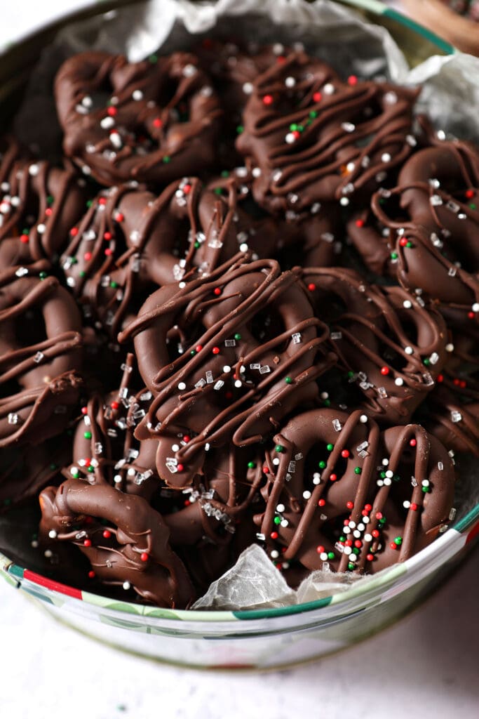 Close up of chocolate dipped pretzels drizzled with extra chocolate and decorated with red, white and green sprinkles in a tin