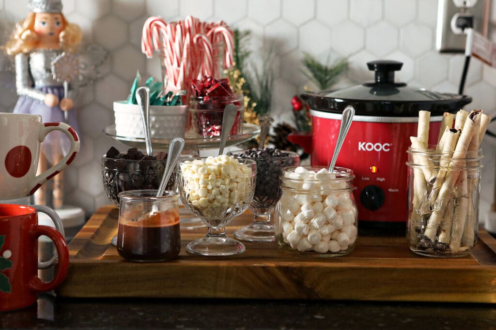 A hot chocolate bar on a countertop with various toppings and a small slow cooker of hot cocoa