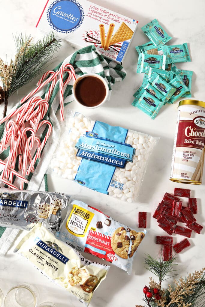 Ingredients to make a hot chocolate bar on a white surface with pine needles