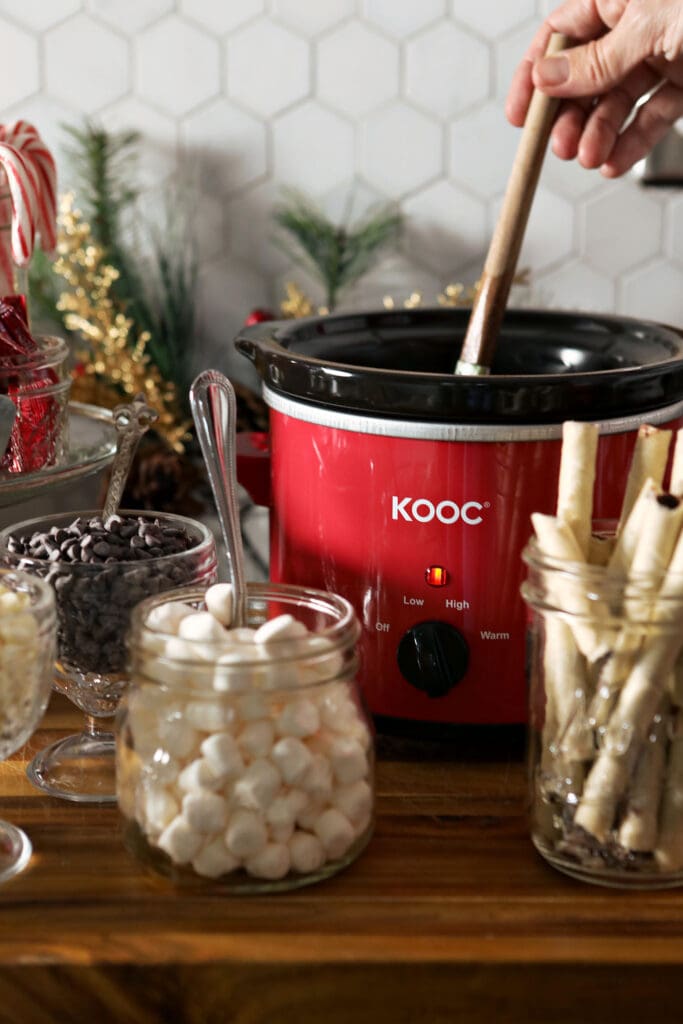 A hand stirs a slow cooker of hot chocolate on a hot chocolate board