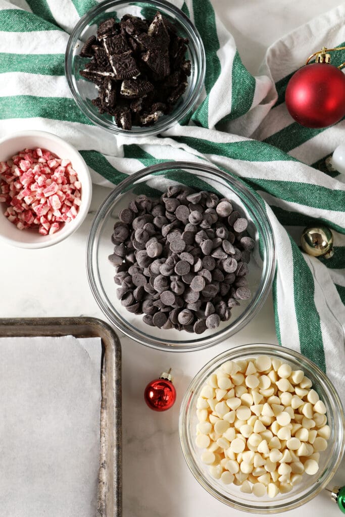 Ingredients to make peppermint bark with Oreos in bowls with a green and white striped towel and ornaments