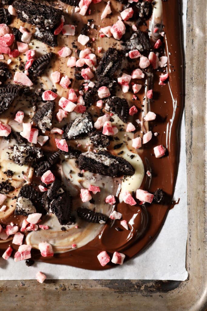 Peppermint crunch and Oreos on top of white and dark chocolate on a sheet pan