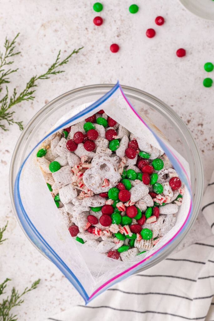 M&Ms and crushed candy canes on top of reindeer chow in a tiptop bag