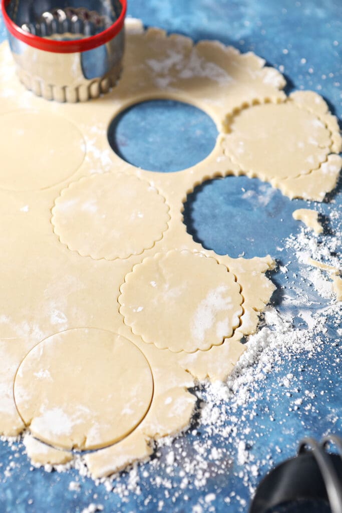 Round cookie cutters cut out cookie dough rolled out on a blue surface