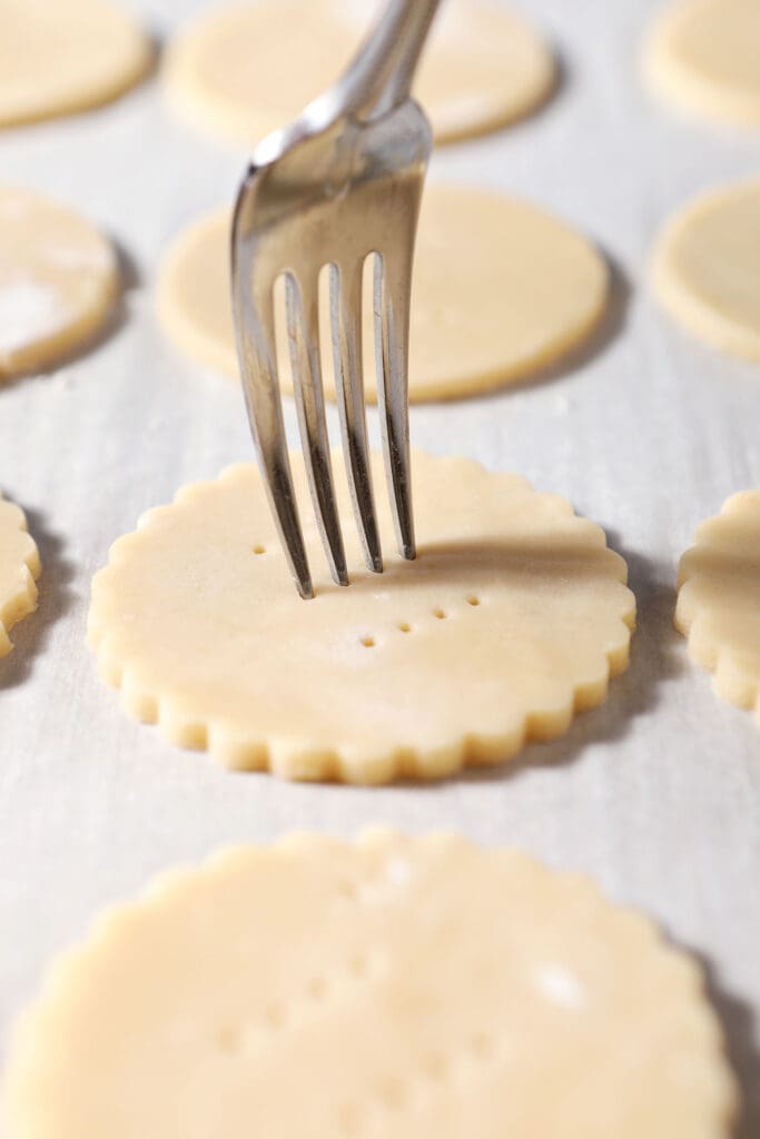 A fork pokes holes into a scalloped shortbread cookie