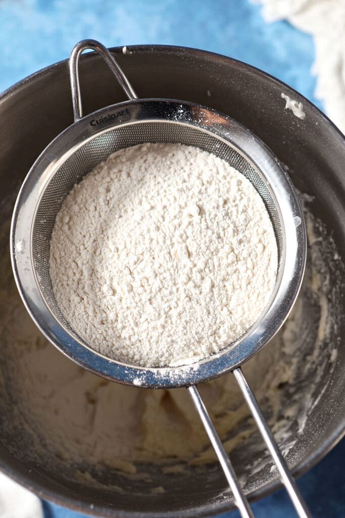 Flour sifts on top of wet ingredients in a metal bowl