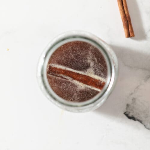 A mason jar holds cinnamon-infused maple syrup with a cinnamon stick inside it