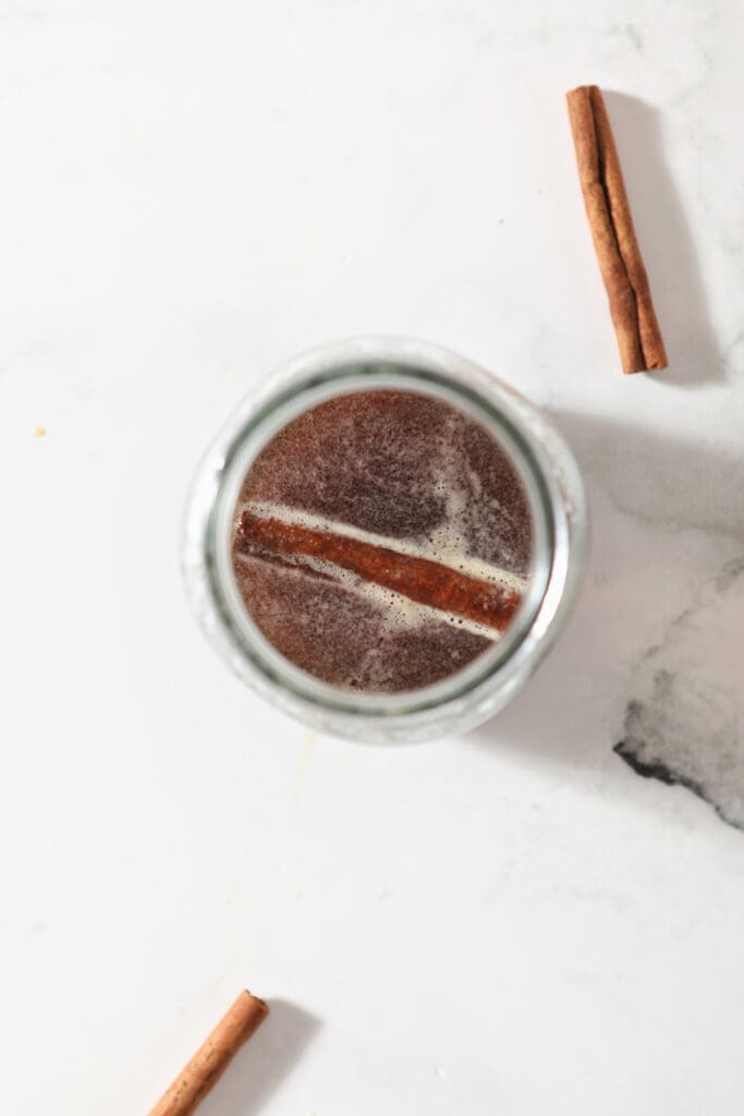 A mason jar holds cinnamon-infused maple syrup with a cinnamon stick inside it