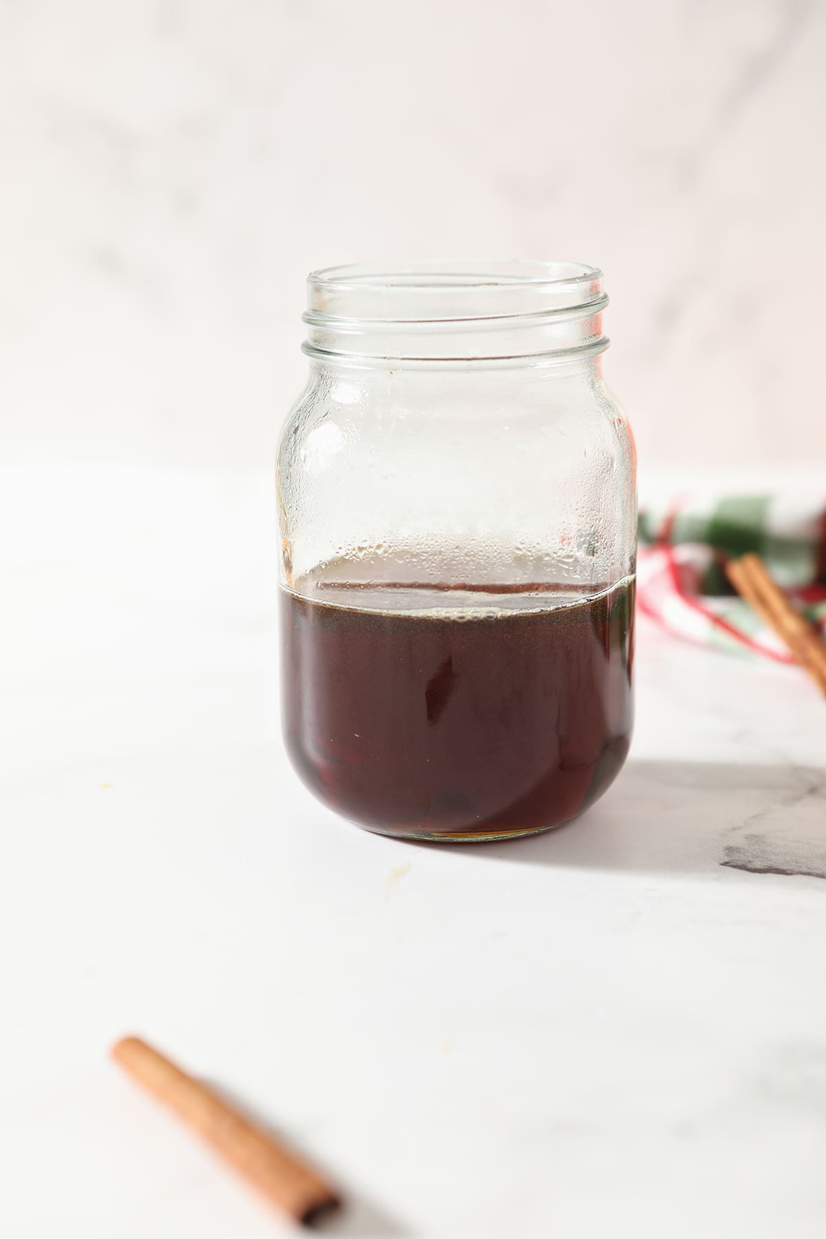 A mason jar holds cinnamon-infused maple syrup on a marble surface