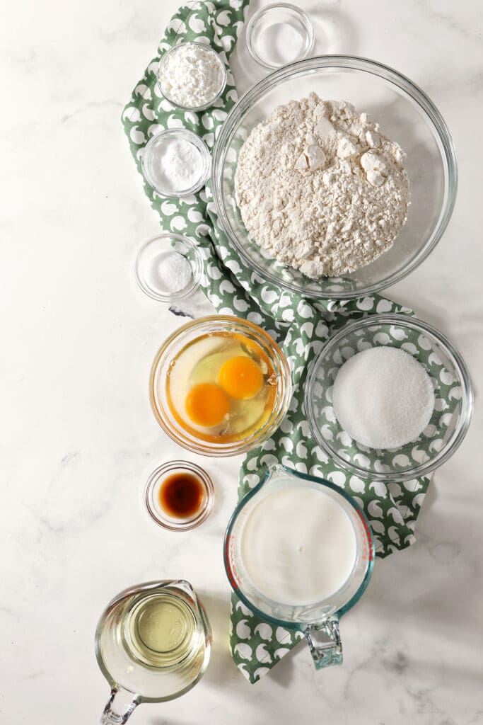 Ingredients to make waffles in bowls on a marble surface with a patterned green towel