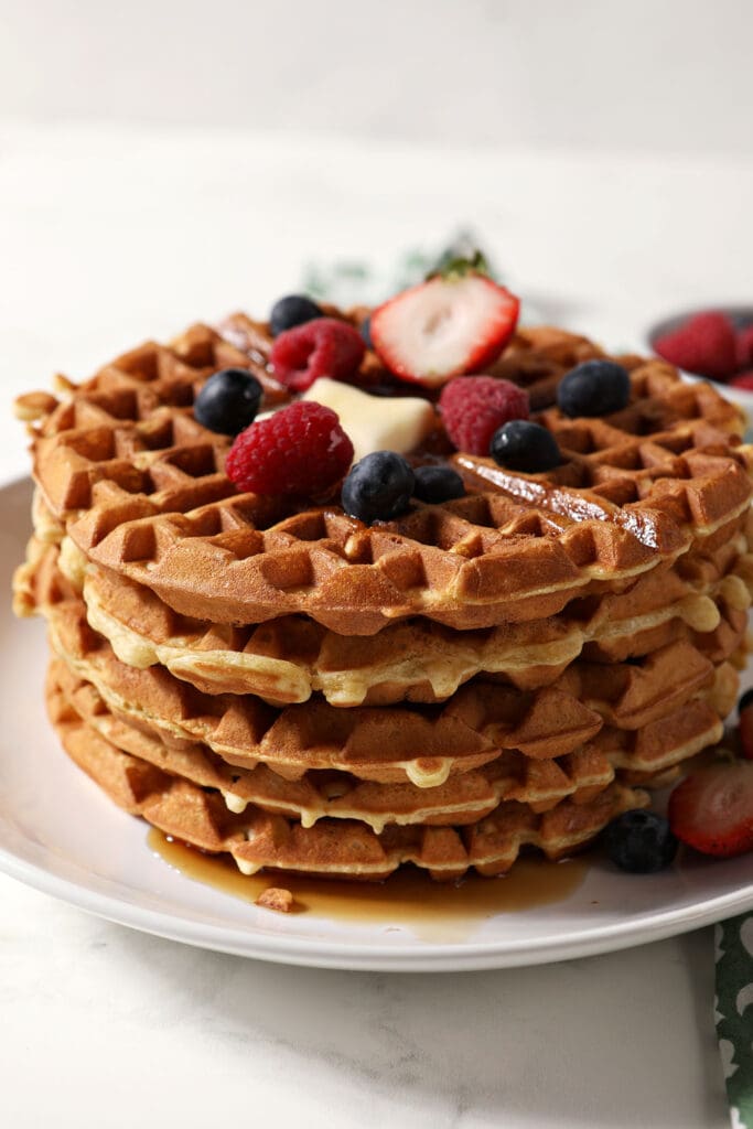 A stack of waffles on a white plate topped with berries