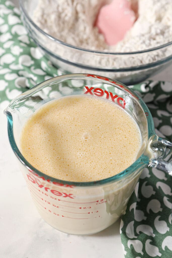 Wet ingredients for waffles in a liquid measuring cup on marble next to a green patterned linen