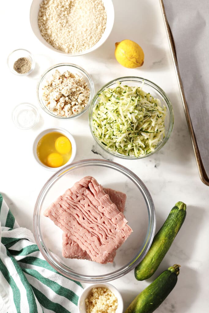 Ingredients to make turkey meatballs with zucchini in bowls on marble