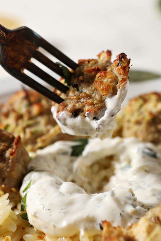 A fork holding a turkey zucchini meatball lifts out of a tzatziki-pasta mixture