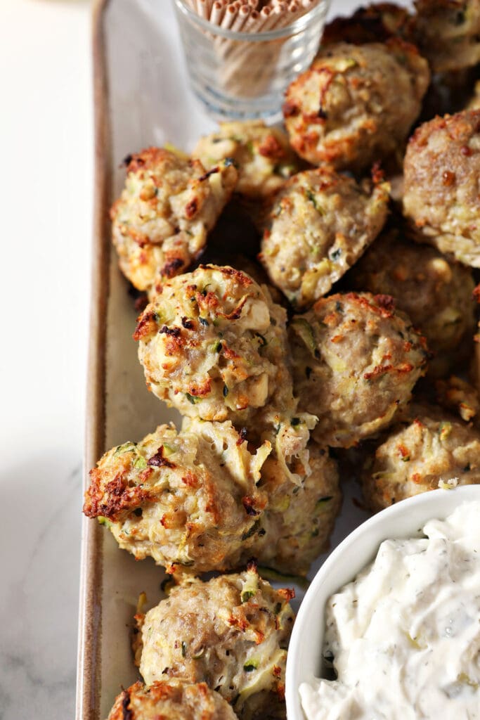 Baked turkey meatballs with zucchini on a plate with tzatziki sauce