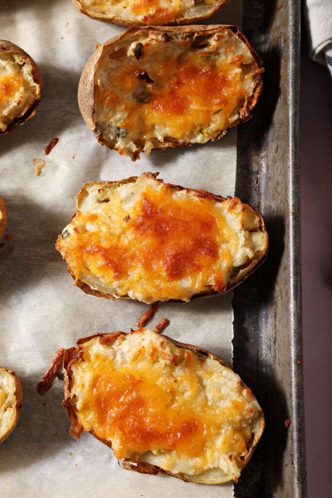 Twice baked potatoes covered in gooey cheese on a sheet pan after baking