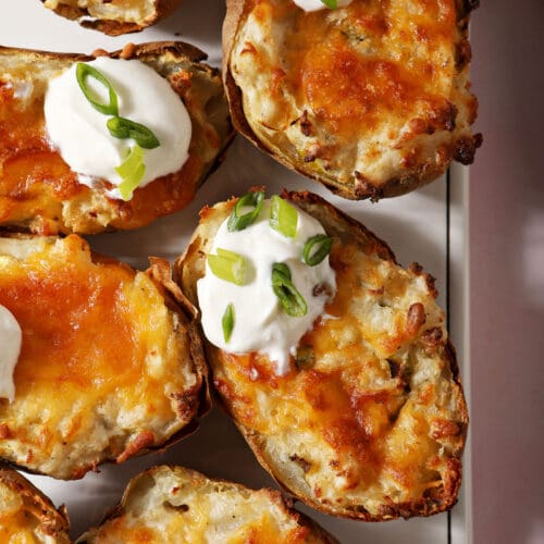 Twice baked potatoes garnished with sour cream and scallions on a white platter