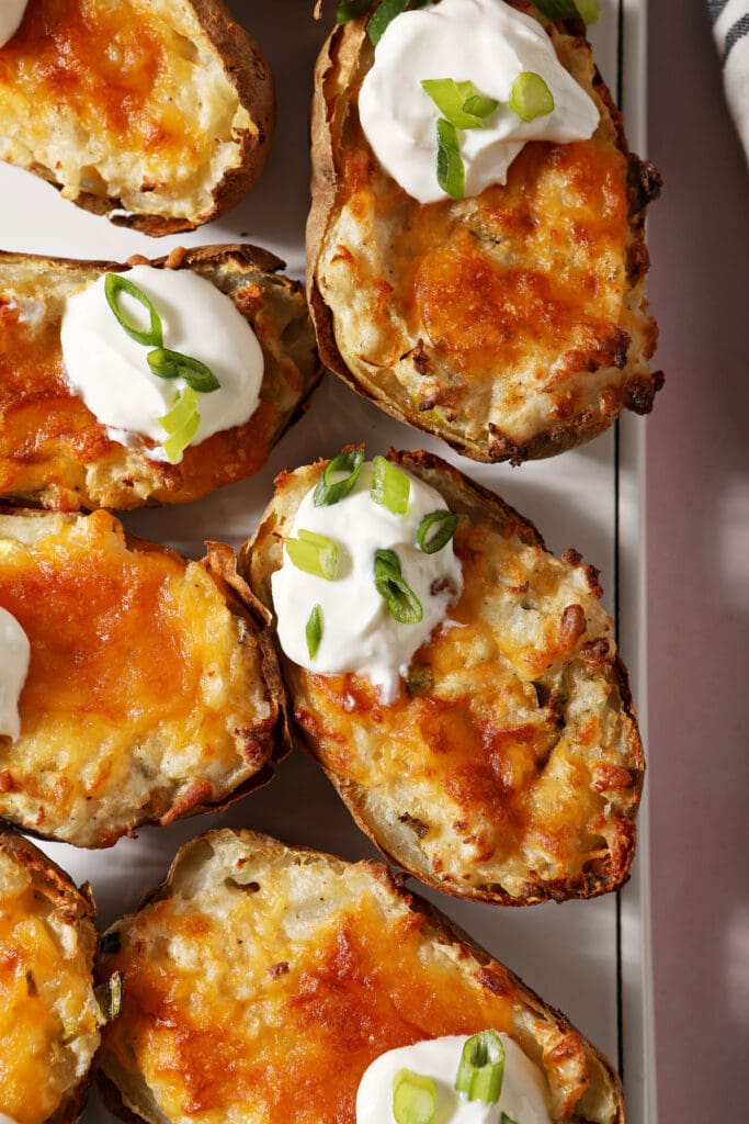 Twice baked potatoes garnished with sour cream and scallions on a white platter