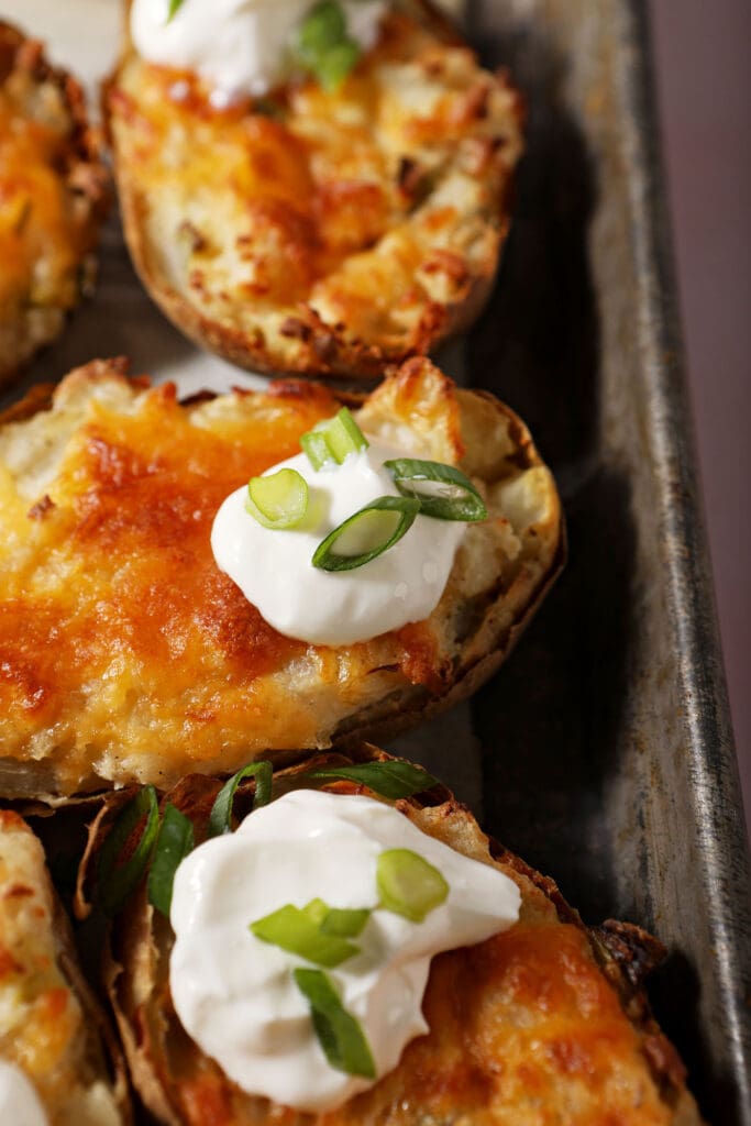 Close up of a few twice baked potatoes on a metal pan garnished with sour cream and scallions