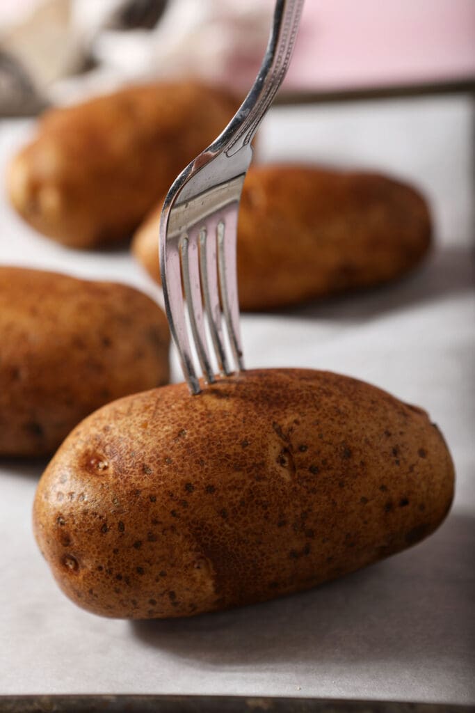 A fork pierces a potato on a sheet pan