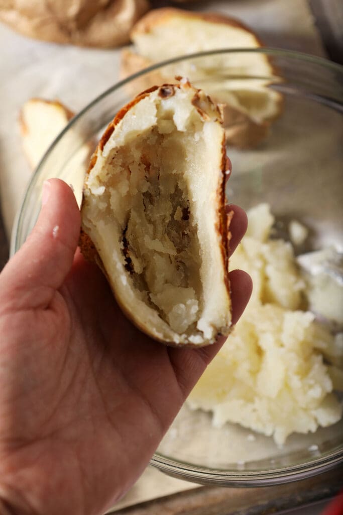 A scooped out potato skin is held in hand above a bowl