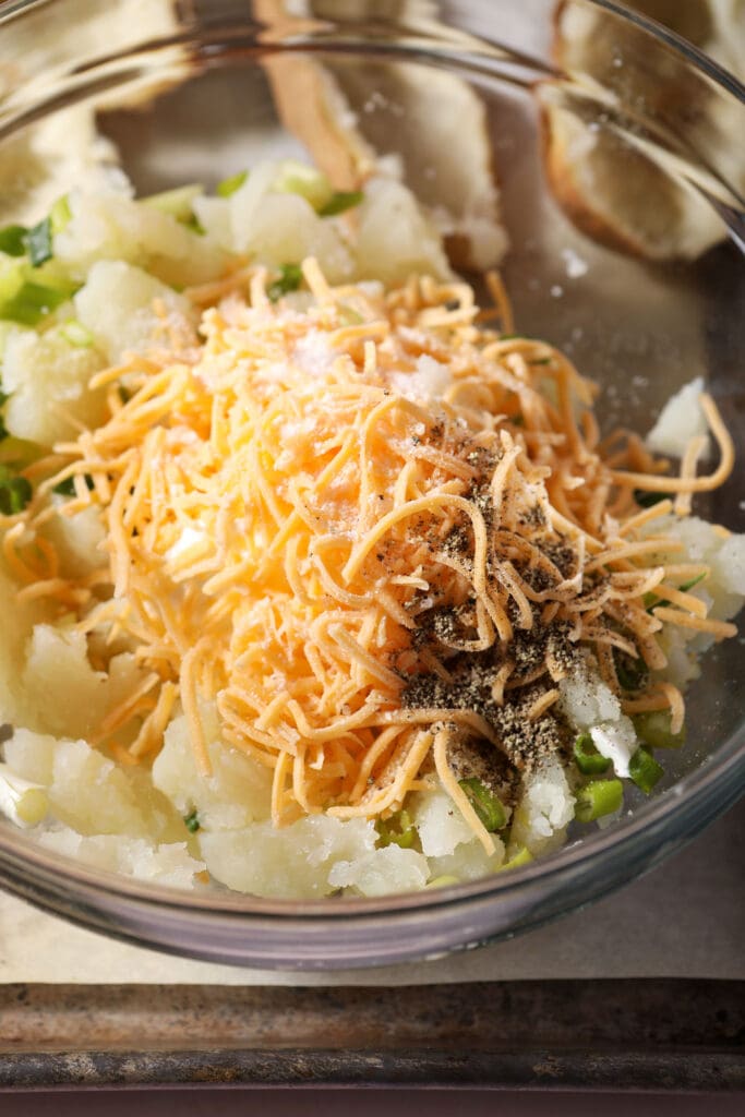 Cheese, sour cream, green onions, potato and more in a bowl before mixing