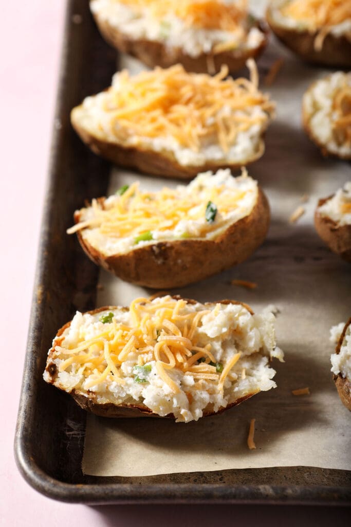 Twice baked potatoes topped with shredded cheese on a pan before baking