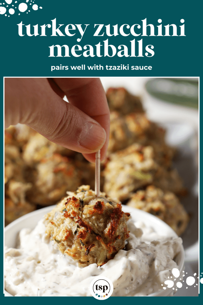 A Turkey Zucchini Meatball dips in a bowl of tzatziki surrounded by more baked meatballs with the text turkey zucchini meatballs pairs well with tzatziki