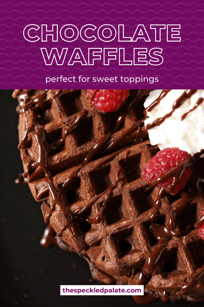 Overhead of a chocolate waffle drizzled with chocolate sauce, strawberries and whipped cream on a black plate with the text chocolate waffles perfect for sweet toppings