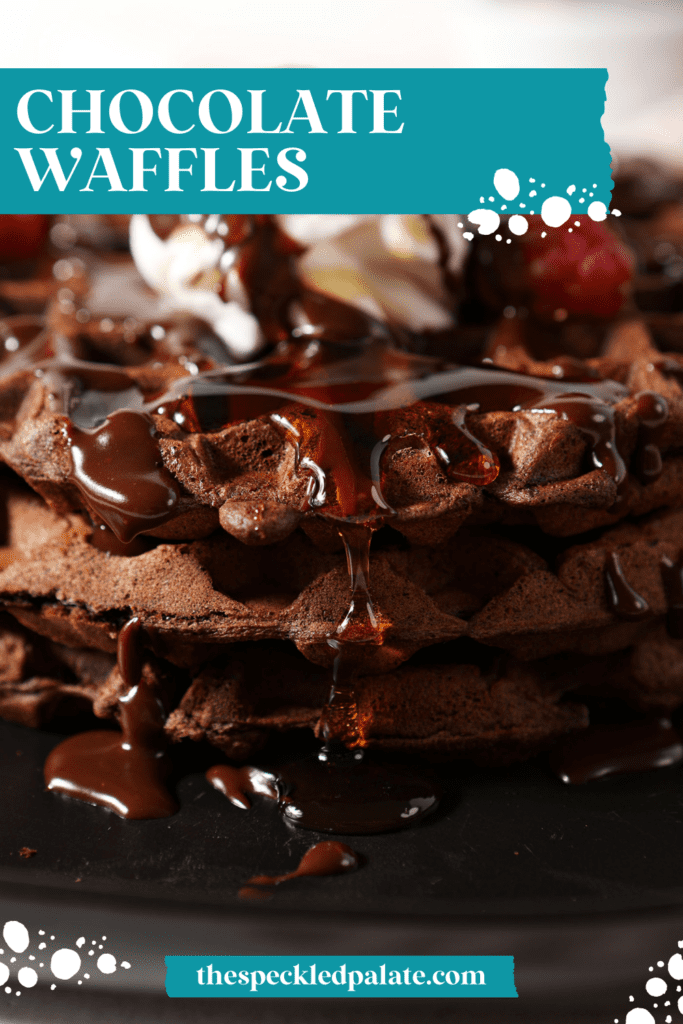 Close up of maple syrup dripping down a stack of chocolate waffles topped with whipped cream, raspberries and chocolate sauce with the text chocolate waffles