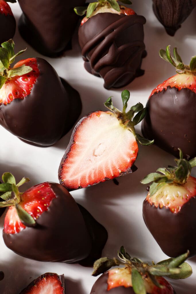 Whole and halved chocolate dipped strawberries on a white platter