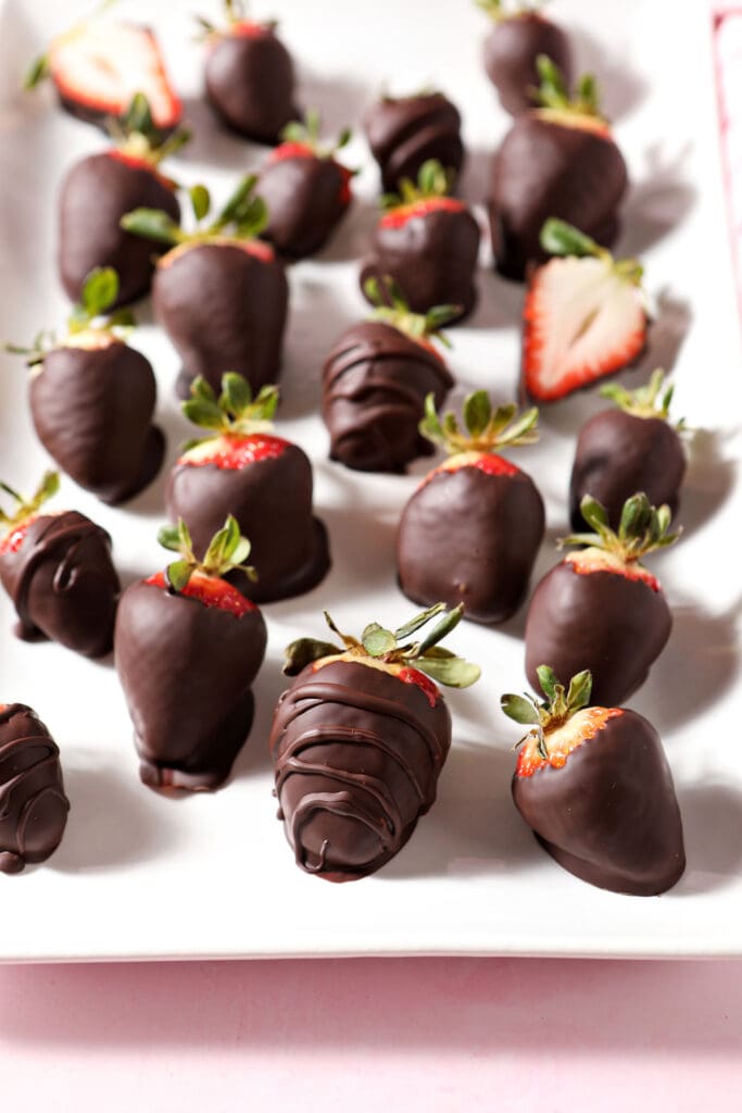 Chocolate covered strawberries on a white platter on a pink surface