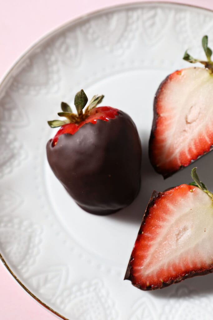 Close up of a whole chocolate covered strawberry and two halved ones on a white plate