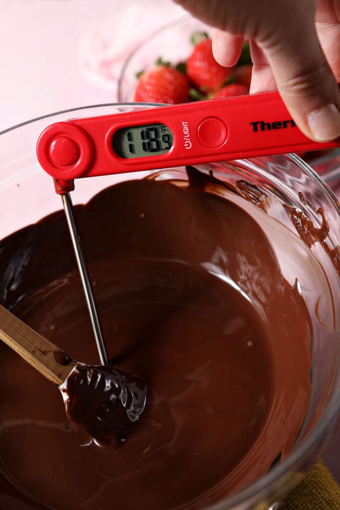 A red instant read thermometer takes the temperature of chocolate, which reads 118