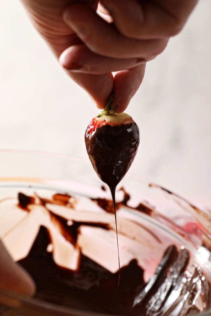 Melted chocolate drizzles off a strawberry over a bowl