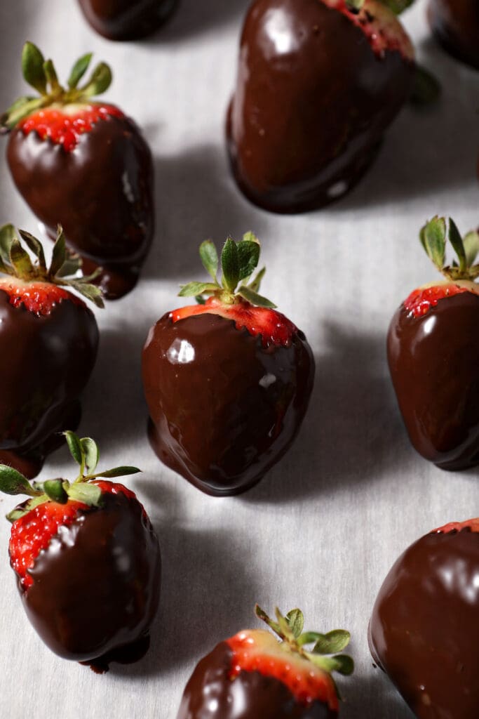 Shiny chocolate dipped strawberries on a parchment-lined sheet pan