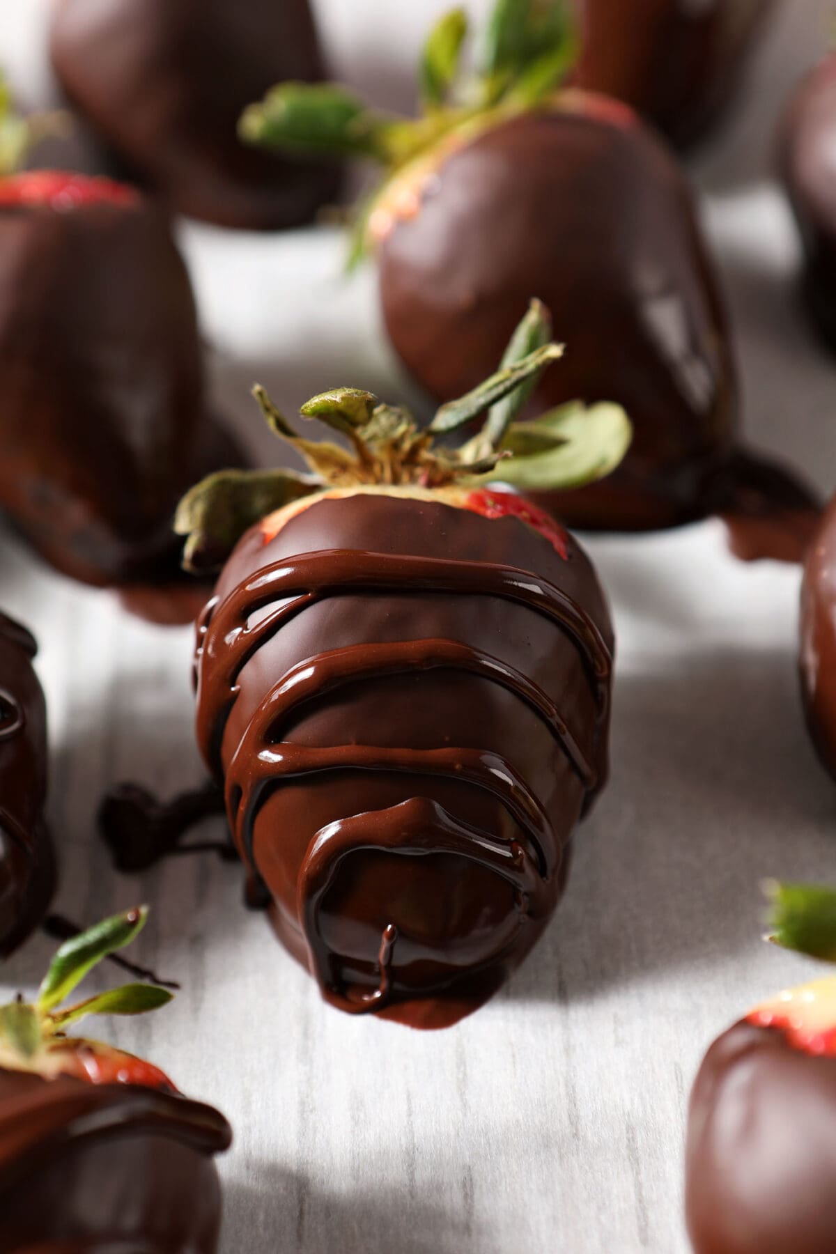 Close up of a chocolate covered strawberry with an extra drizzle of chocolate on parchment