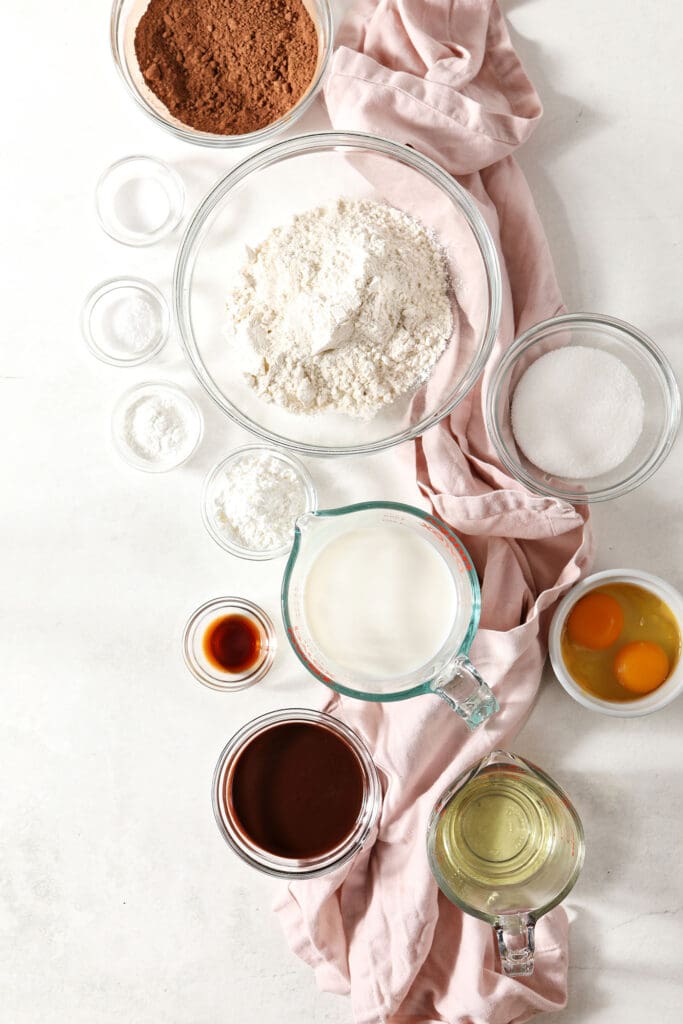 Ingredient to make homemade chocolate waffles in bowls and cups on a marble surface with pink linens