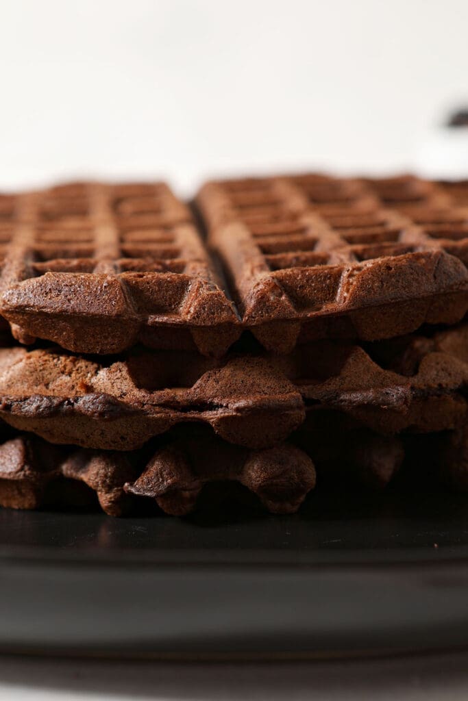 A stack of three chocolate waffles on a black plate