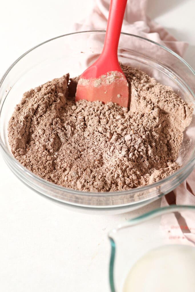 Dry waffle ingredients in a bowl with a red spatula on marble