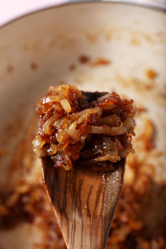 A wooden spoon holds a serving of caramelized onions over a skillet