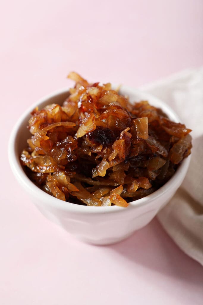 A bowl of caramelized onions on a pink surface next to a white linen